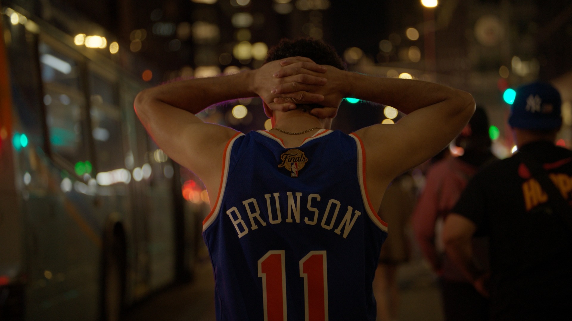 A Knicks fan in a Brunson jersey reacting in a nighttime crowd