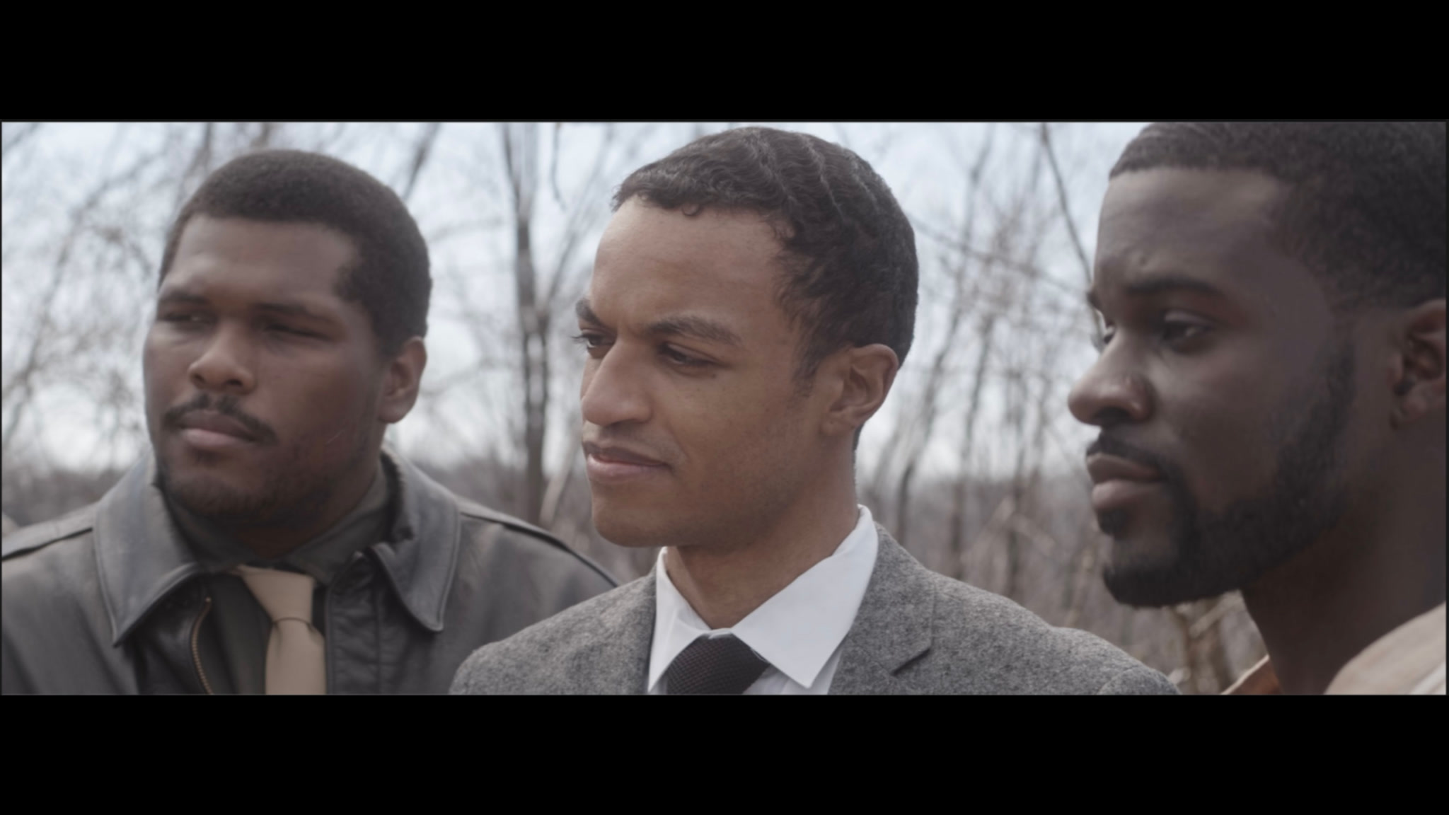 Three men standing together outdoors in a scene from Lineage
