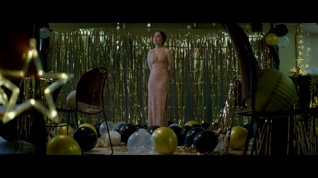 A woman in a formal dress standing alone among balloons after a party